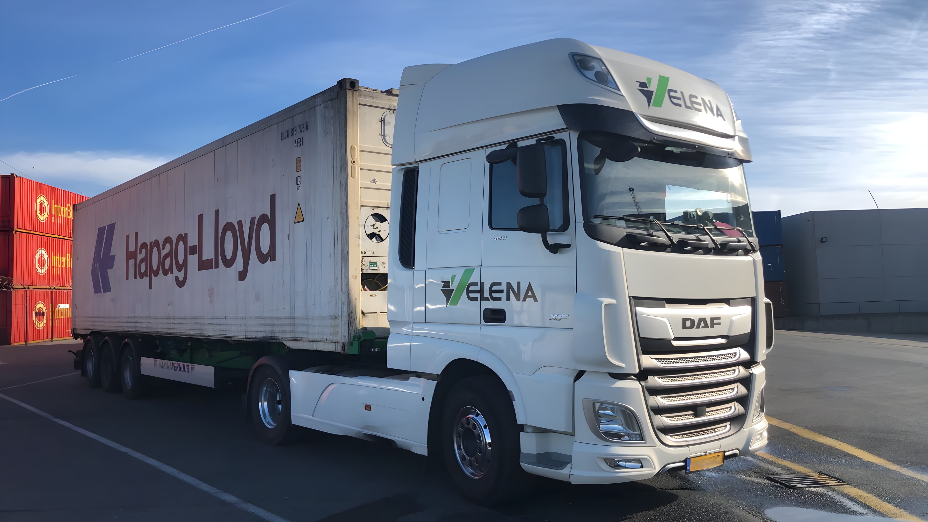 White DAF semi truck with Elena branding hauling a Hapag-Lloyd container in a shipping yard.