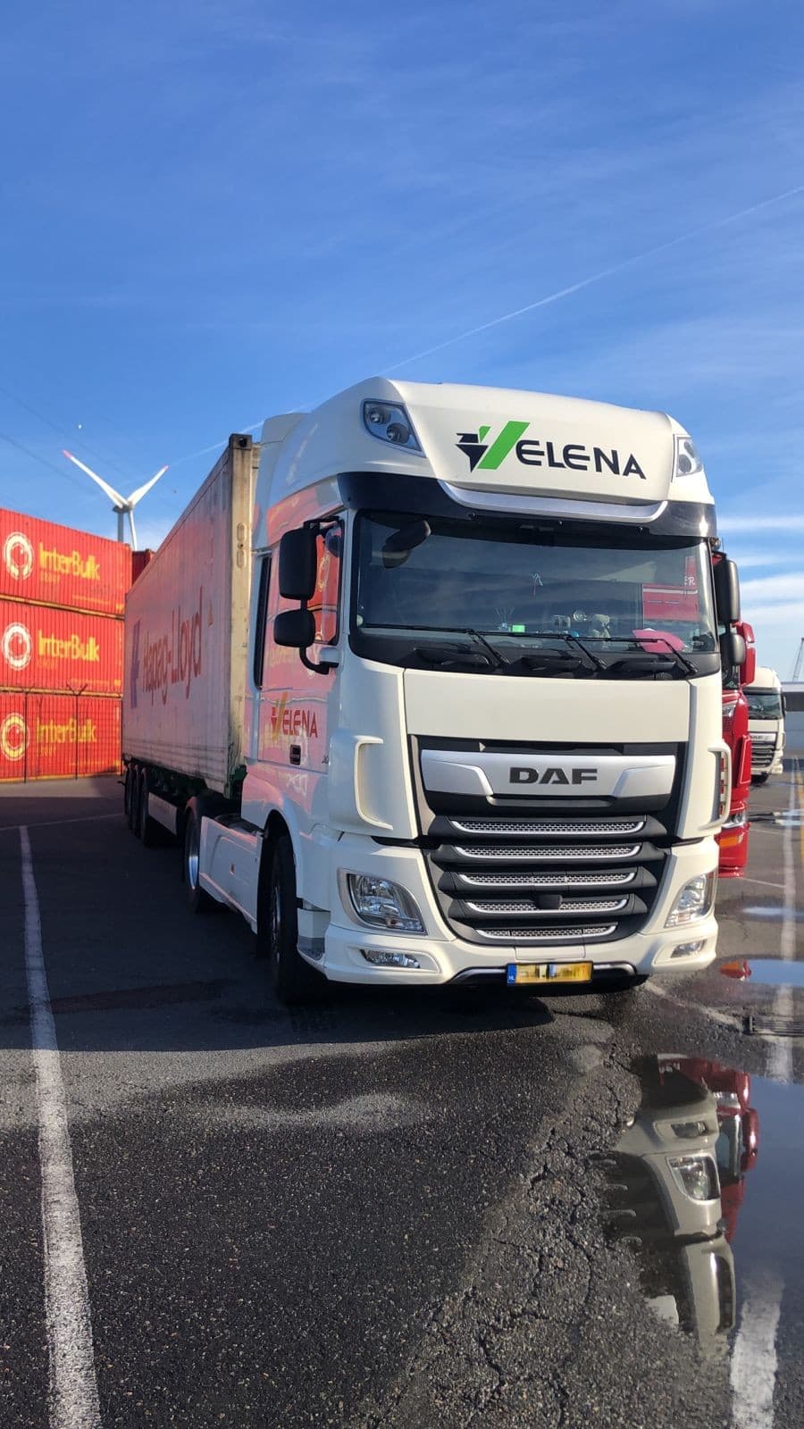 White DAF truck with Elena branding parked near red shipping containers and a wind turbine.